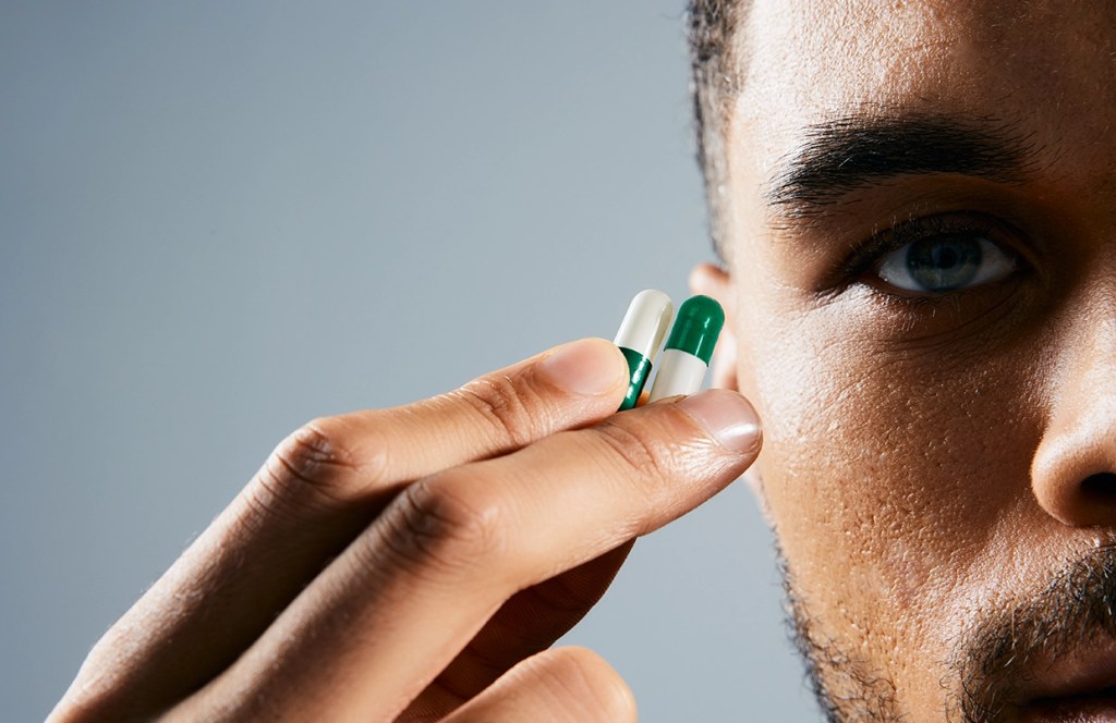 Man holding two capsules looking closely